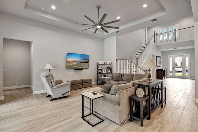 living room with a raised ceiling, french doors, a high ceiling, and ceiling fan