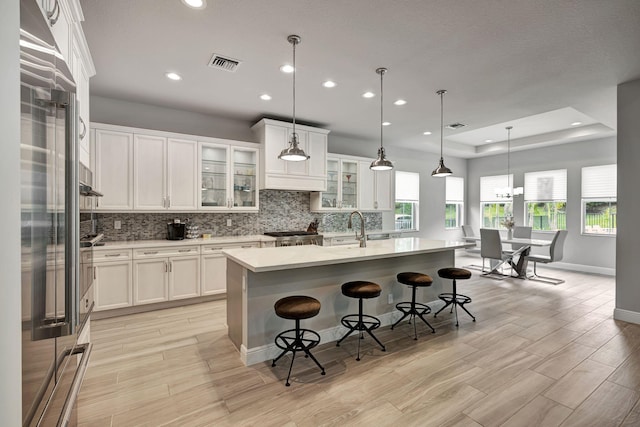 kitchen with a raised ceiling, a kitchen bar, a center island with sink, and hanging light fixtures