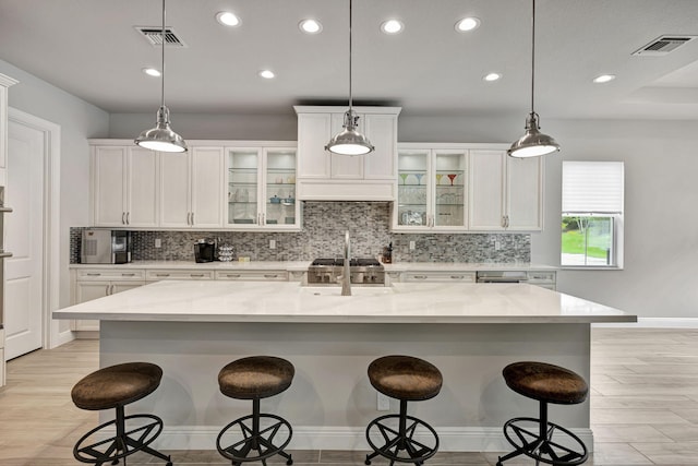 kitchen with white cabinets, a kitchen bar, hanging light fixtures, a large island, and light stone counters