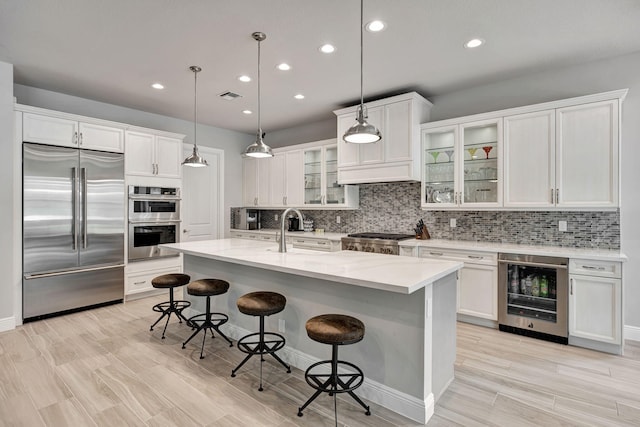 kitchen featuring pendant lighting, beverage cooler, appliances with stainless steel finishes, white cabinetry, and a kitchen island with sink