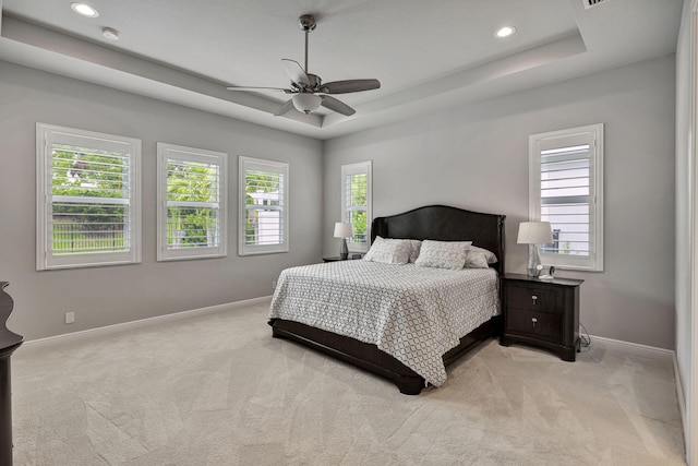 bedroom with a raised ceiling, ceiling fan, and light carpet