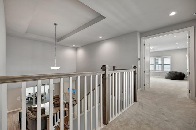 hall with a raised ceiling and light carpet