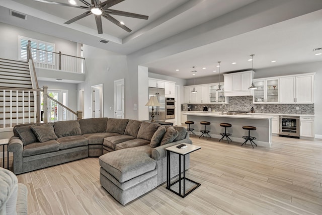 living room with ceiling fan, wine cooler, a high ceiling, and sink