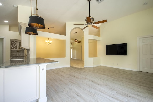 kitchen featuring light wood finished floors, dark stone countertops, white cabinetry, a sink, and ceiling fan with notable chandelier