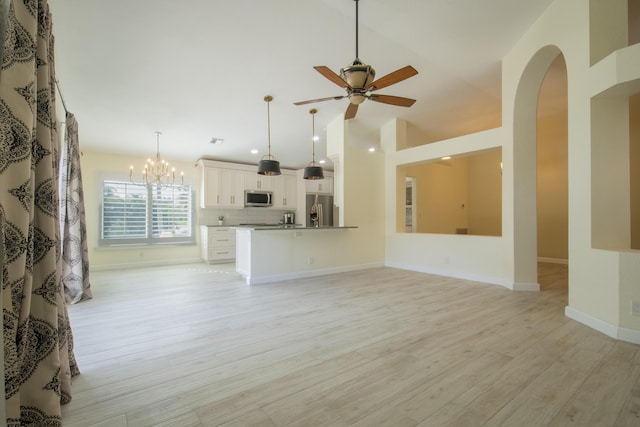 unfurnished living room with arched walkways, baseboards, light wood-style flooring, high vaulted ceiling, and ceiling fan with notable chandelier