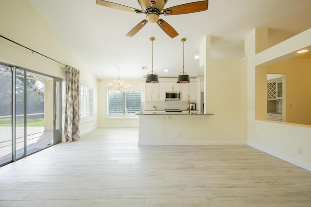 unfurnished living room featuring lofted ceiling, baseboards, light wood finished floors, and ceiling fan with notable chandelier