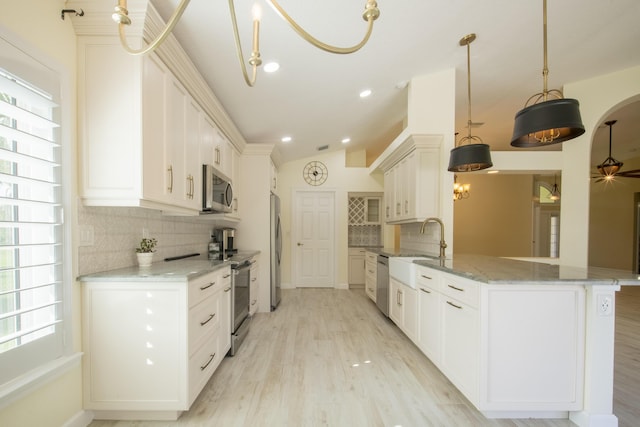 kitchen featuring light wood finished floors, appliances with stainless steel finishes, vaulted ceiling, light stone countertops, and a peninsula