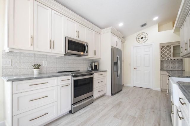 kitchen featuring white cabinetry, vaulted ceiling, stainless steel appliances, and dark stone countertops