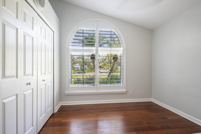 unfurnished bedroom featuring multiple windows, baseboards, dark wood finished floors, and a closet