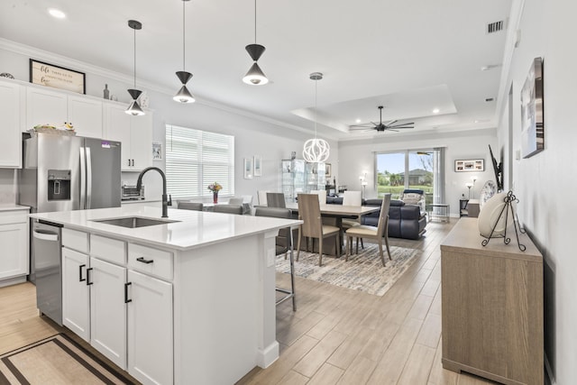 kitchen with sink, appliances with stainless steel finishes, white cabinets, a center island with sink, and a raised ceiling