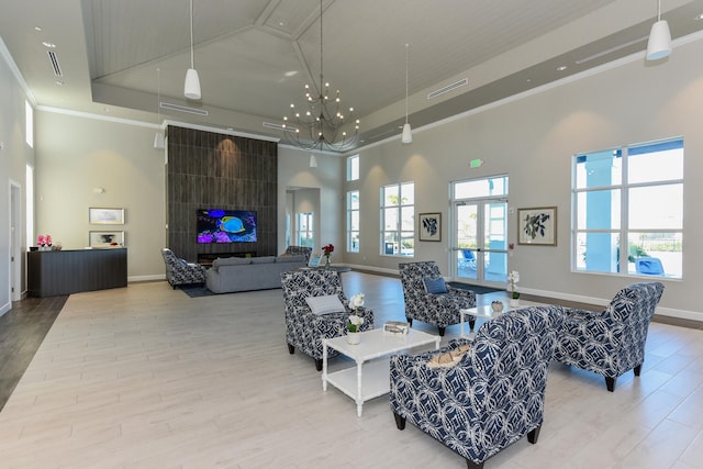 living room with a tile fireplace, a high ceiling, ornamental molding, light hardwood / wood-style floors, and a tray ceiling