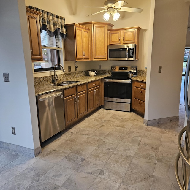 kitchen with appliances with stainless steel finishes, sink, dark stone countertops, and ceiling fan