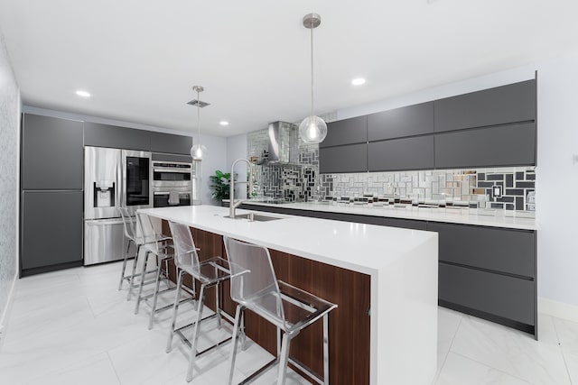 kitchen with appliances with stainless steel finishes, tasteful backsplash, a kitchen island with sink, pendant lighting, and sink