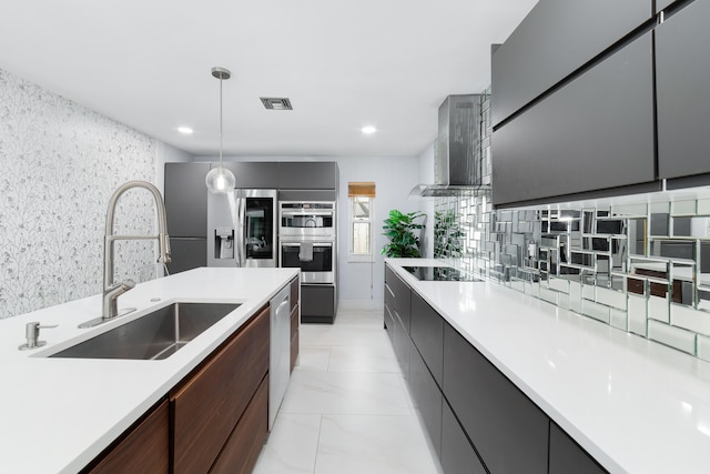 kitchen with pendant lighting, appliances with stainless steel finishes, wall chimney range hood, sink, and backsplash