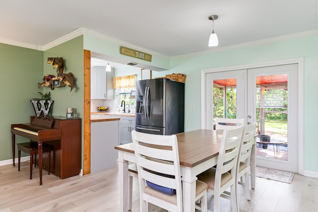 dining space featuring ornamental molding, sink, light hardwood / wood-style floors, and french doors