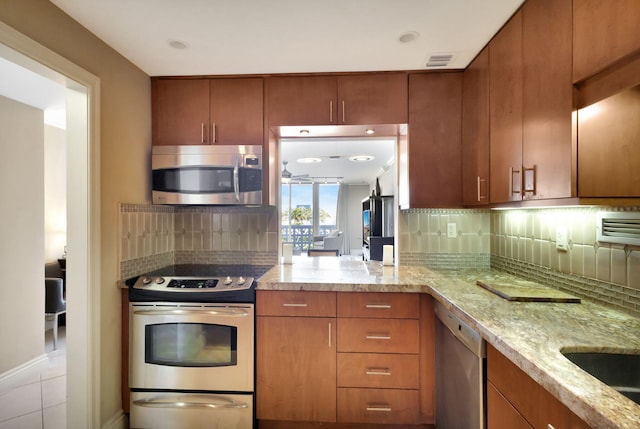 kitchen with light stone counters, backsplash, kitchen peninsula, and appliances with stainless steel finishes