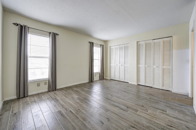 unfurnished bedroom featuring multiple closets, a textured ceiling, and light wood-type flooring