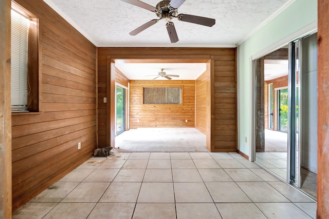 hall featuring light tile patterned flooring, crown molding, a textured ceiling, and wood walls