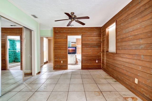 unfurnished room featuring light tile patterned flooring, ceiling fan, a textured ceiling, and wood walls