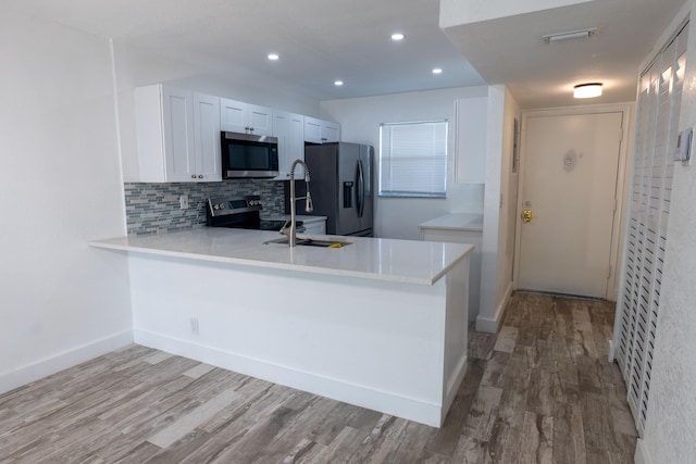 kitchen featuring white cabinets, appliances with stainless steel finishes, backsplash, kitchen peninsula, and light hardwood / wood-style flooring