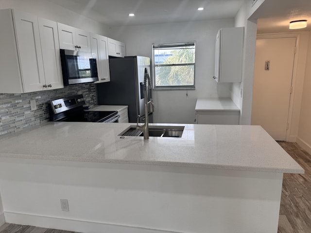 kitchen featuring tasteful backsplash, kitchen peninsula, sink, white cabinetry, and stainless steel appliances