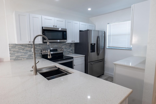 kitchen featuring light stone countertops, white cabinets, stainless steel appliances, tasteful backsplash, and sink