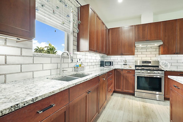 kitchen featuring stainless steel gas range oven, sink, backsplash, and light stone counters