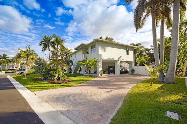 view of front facade featuring stairway, a front yard, stucco siding, decorative driveway, and a carport