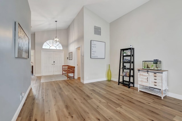 foyer with high vaulted ceiling, an inviting chandelier, and light hardwood / wood-style floors