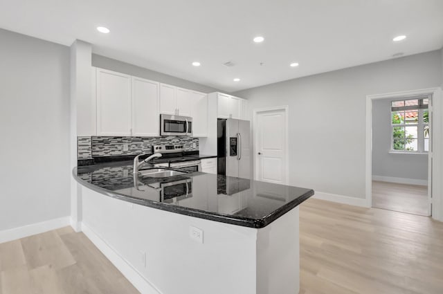 kitchen with white cabinetry, stainless steel appliances, kitchen peninsula, and dark stone counters