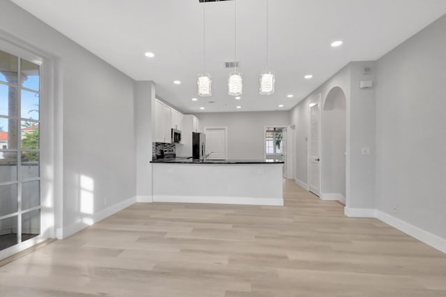 kitchen featuring appliances with stainless steel finishes, pendant lighting, white cabinets, light hardwood / wood-style floors, and kitchen peninsula