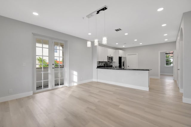 kitchen featuring appliances with stainless steel finishes, pendant lighting, white cabinetry, light hardwood / wood-style floors, and kitchen peninsula