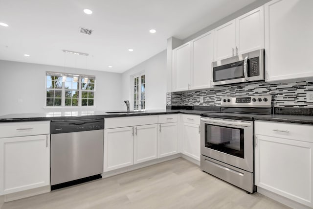 kitchen featuring sink, appliances with stainless steel finishes, white cabinetry, decorative backsplash, and light wood-type flooring