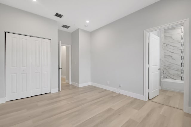 unfurnished bedroom with connected bathroom, light wood-type flooring, and a closet