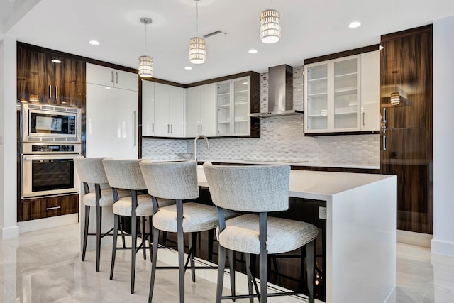 kitchen featuring pendant lighting, stainless steel appliances, a center island with sink, and wall chimney range hood