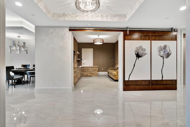 hallway with a raised ceiling, a barn door, and a chandelier