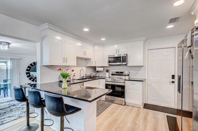 kitchen featuring kitchen peninsula, light wood-type flooring, a breakfast bar area, stainless steel appliances, and white cabinets