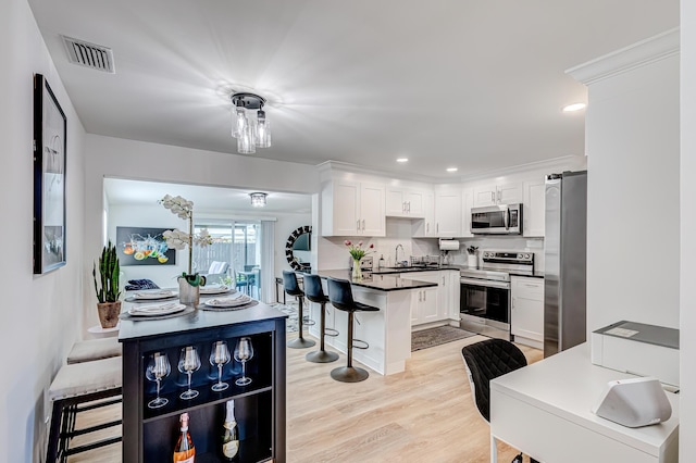 kitchen with tasteful backsplash, kitchen peninsula, white cabinetry, appliances with stainless steel finishes, and a kitchen breakfast bar