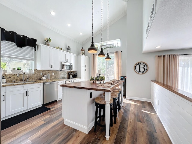 kitchen with butcher block counters, appliances with stainless steel finishes, ornamental molding, white cabinets, and sink