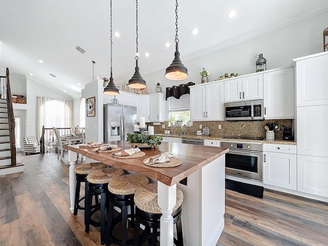 kitchen with lofted ceiling, pendant lighting, decorative backsplash, stainless steel appliances, and white cabinets