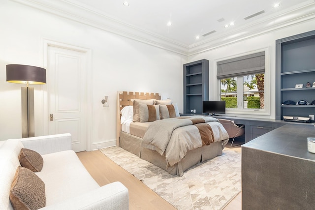 bedroom with built in desk, crown molding, and light hardwood / wood-style flooring