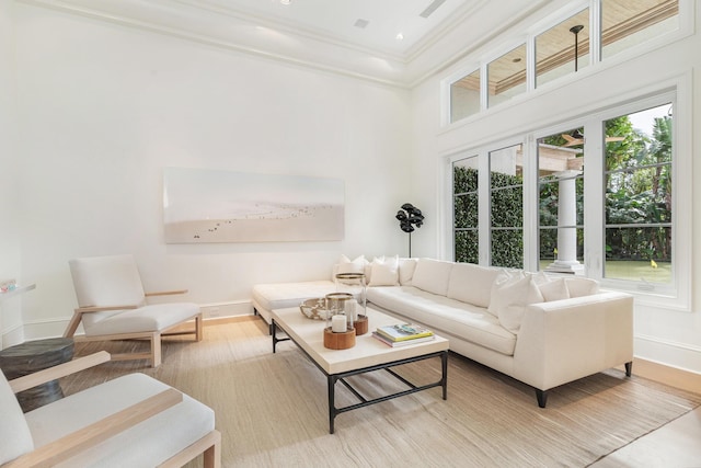 living room with a towering ceiling, ornamental molding, and light hardwood / wood-style flooring