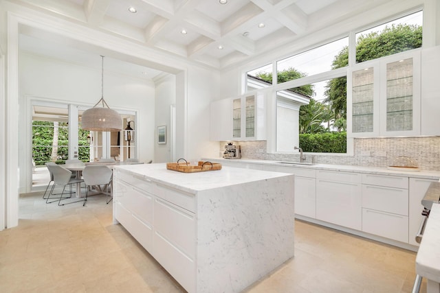 kitchen with a high ceiling, a kitchen island, white cabinetry, sink, and hanging light fixtures