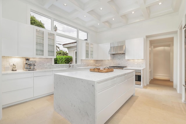 kitchen featuring white cabinets, a center island, wall chimney exhaust hood, sink, and light stone counters