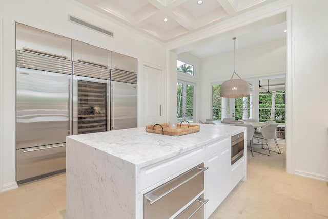 kitchen with white cabinets, a kitchen island, decorative light fixtures, built in appliances, and coffered ceiling