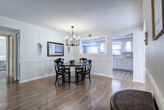 dining room with a textured ceiling, an inviting chandelier, ornamental molding, and light hardwood / wood-style floors