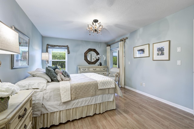 bedroom with light wood-type flooring, a notable chandelier, and a textured ceiling