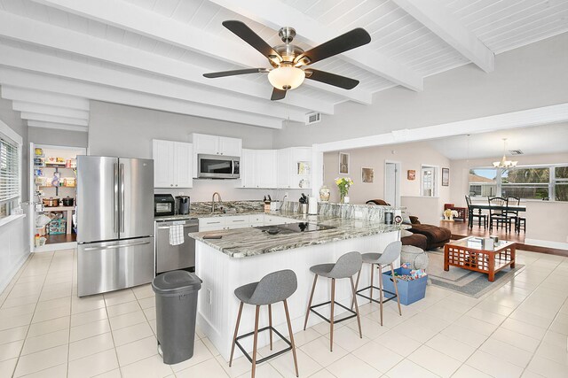 kitchen with a breakfast bar, stainless steel appliances, white cabinets, dark stone counters, and beamed ceiling