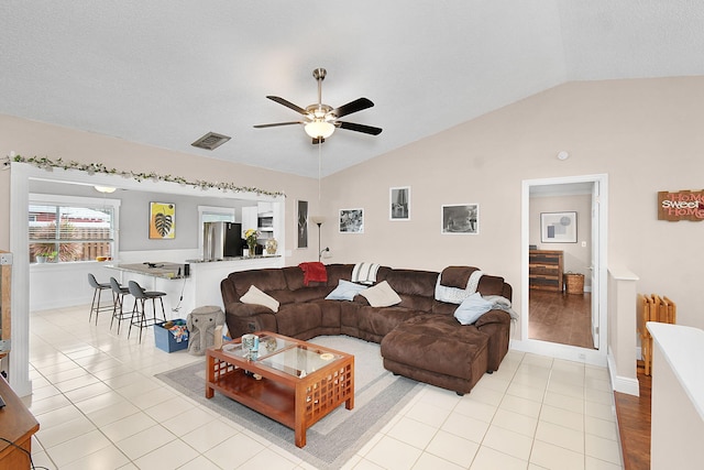 living room featuring light tile patterned flooring, a ceiling fan, visible vents, and lofted ceiling