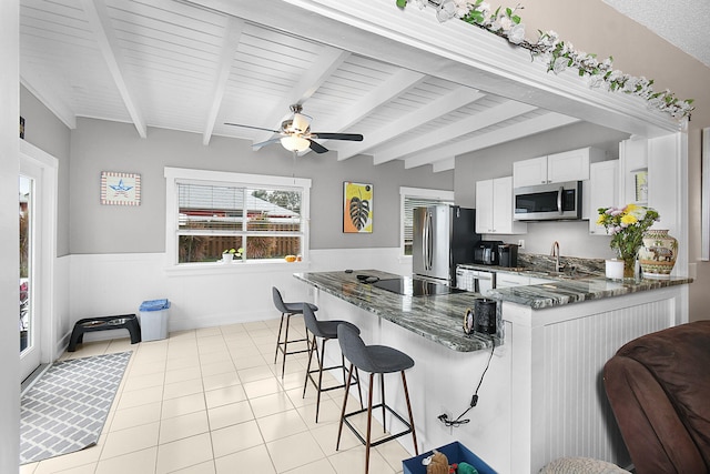 kitchen featuring dark stone countertops, a breakfast bar, stainless steel appliances, white cabinetry, and a wainscoted wall